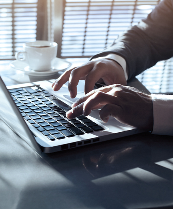 Hands typing on a laptop next to a cup of coffee