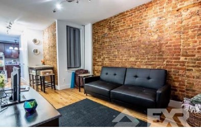 Interior of a living space showing an exposed brick wall with a black couch up against it.